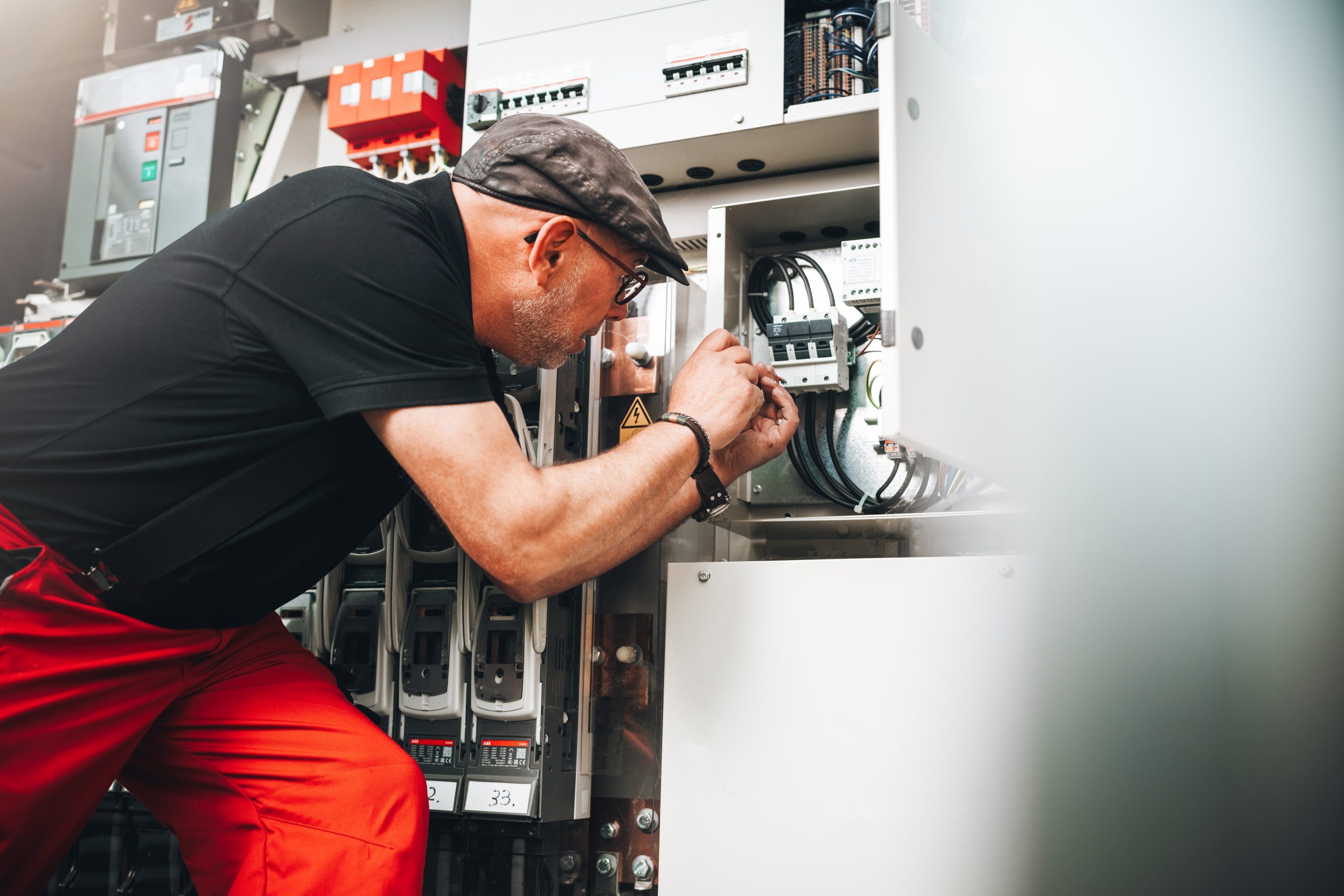 Elektriker in schwarzem Shirt, roter Hose justiert Verkabelung im Schaltschrank.