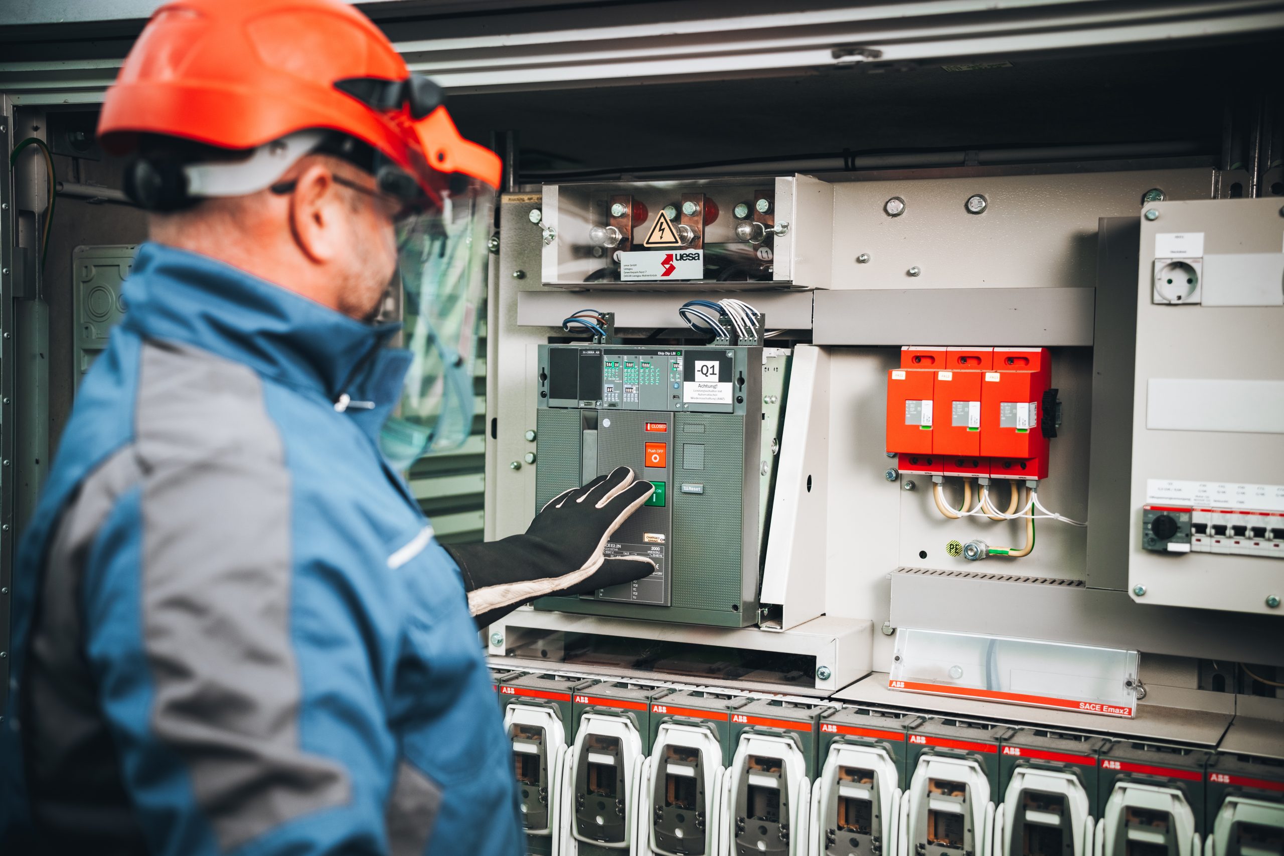 Techniker mit Schutzausrüstung arbeitet am Schaltschrank mit sichtbarer Verkabelung.