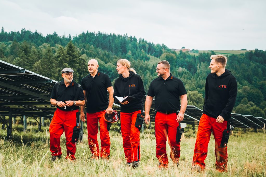 Vier Männer in roten Hosen stehen vor Solarpaneelen und präsentieren Energielösungen