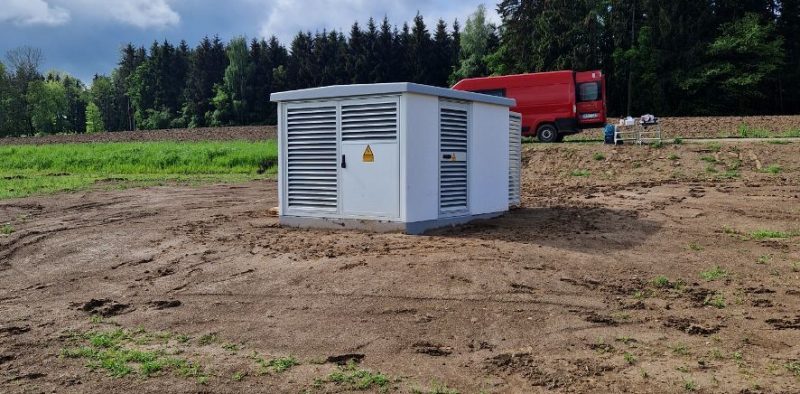 Freistehende Transformatorstation auf freiem Feld mit Erdarbeiten im Hintergrund.