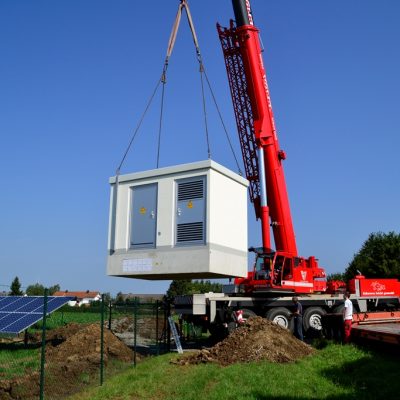 Kran hebt ein weißes Modulgebäude auf eine vorbereitete Fläche.