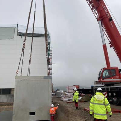 Baustelle mit Kran, der ein großes Modul vor mehreren Arbeitern bewegt